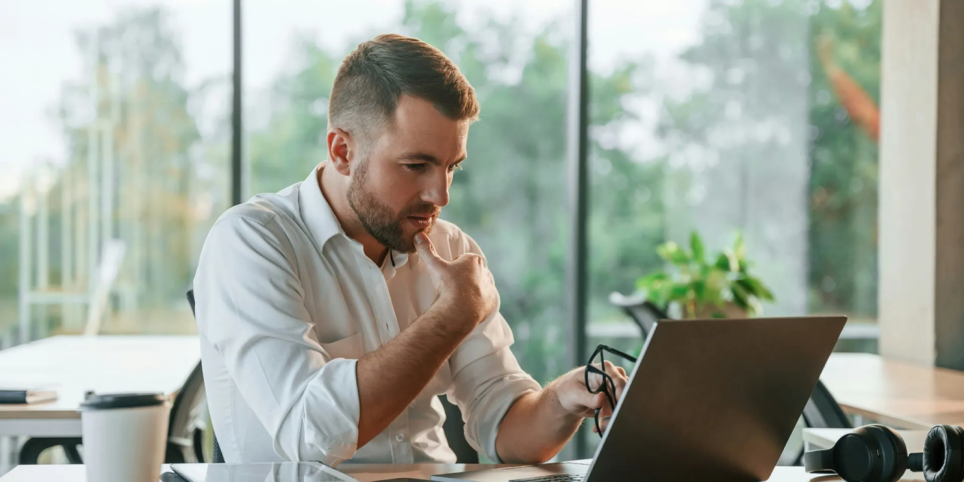 A man in a white shirt thinking while he reviews his laptop